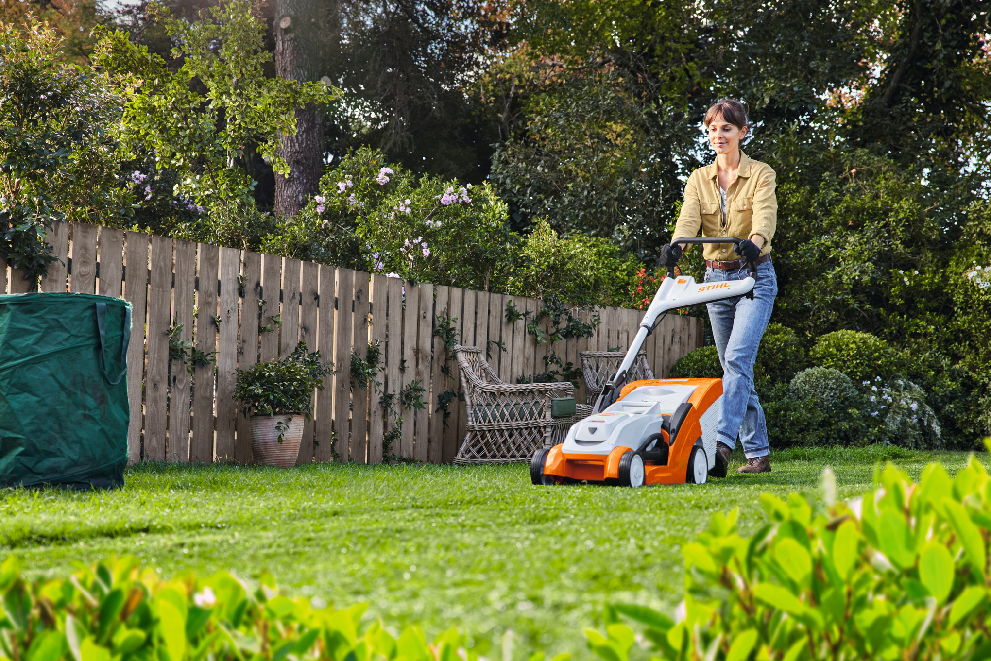 Mann betreibt mit STIHL Rasenmäher RMA 448TC auf einem bewachsenen Grundstück Rasenpflege im Sommer