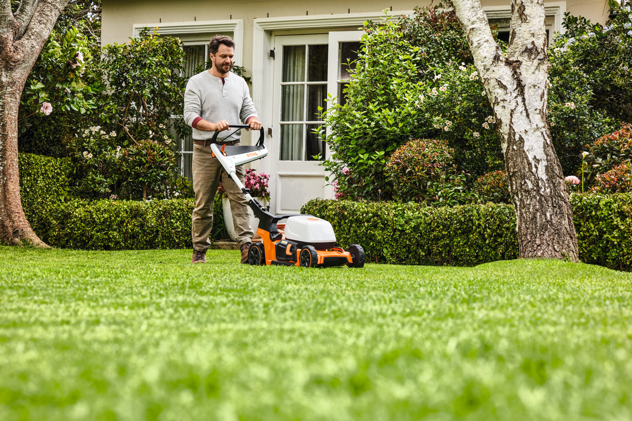 Frau beim Mulchen mit einem STIHL Rasenmäher auf einem grünen Grundstück