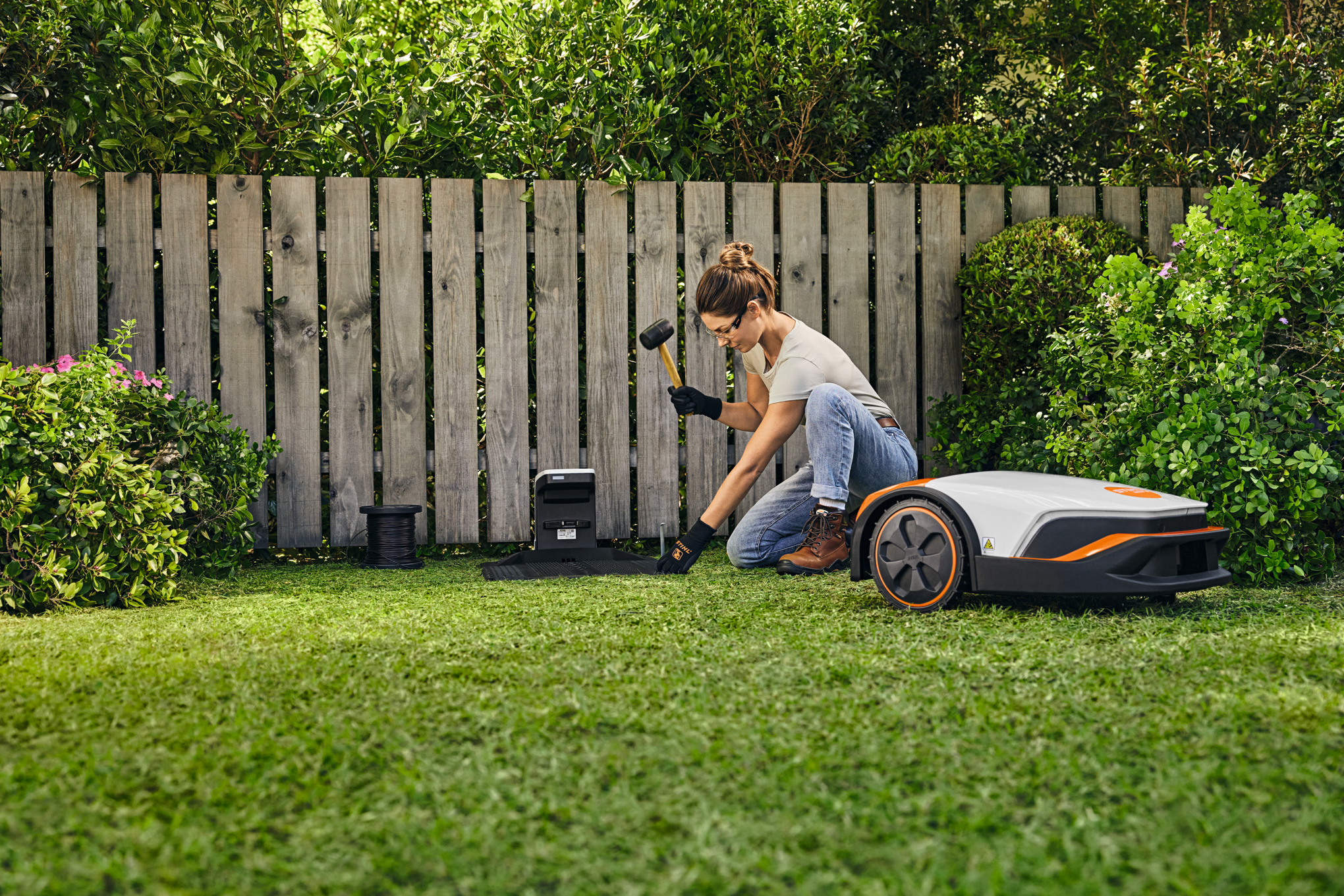 Donna che installa la docking station iMOW® su un terreno da giardino con un martello in mano