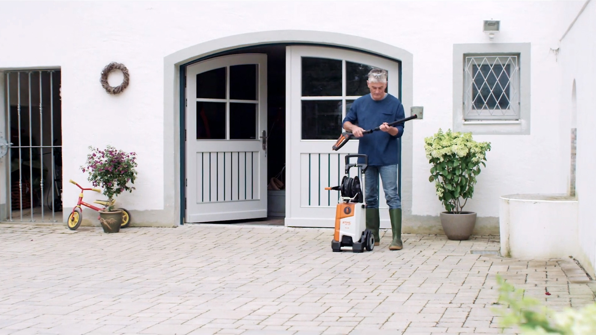 Mann steht vor weissem Haus und bereitet STIHL Hochdruckreiniger vor, um Fassade zu reinigen