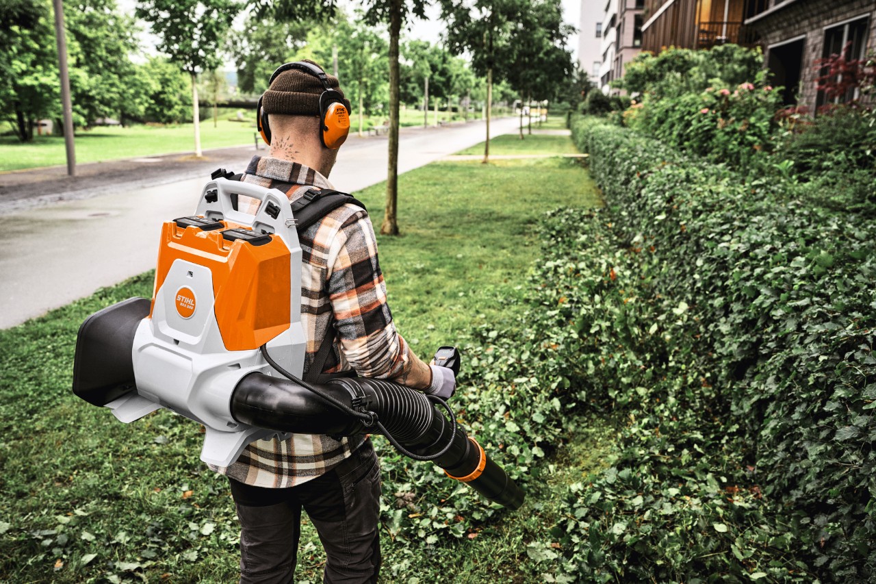 Bediener nutzt den rückentragbaren Akku-Laubbläser STIHL BRA 200 zur Reinigung von Hecken- und Rasenschnitt entlang eines Gehwegs im Gartenbereich