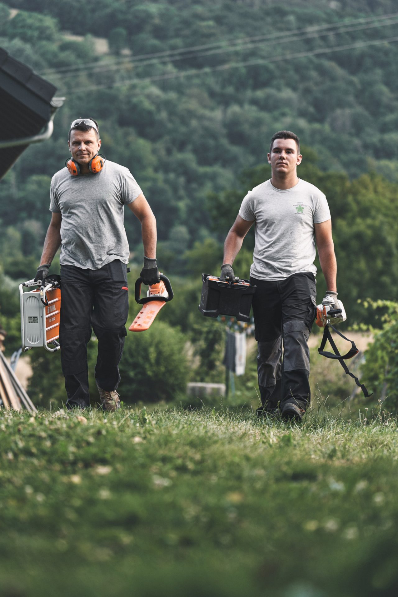 Zwei Profis laufen mit STIHL Akku-Geräten über eine Wiese
