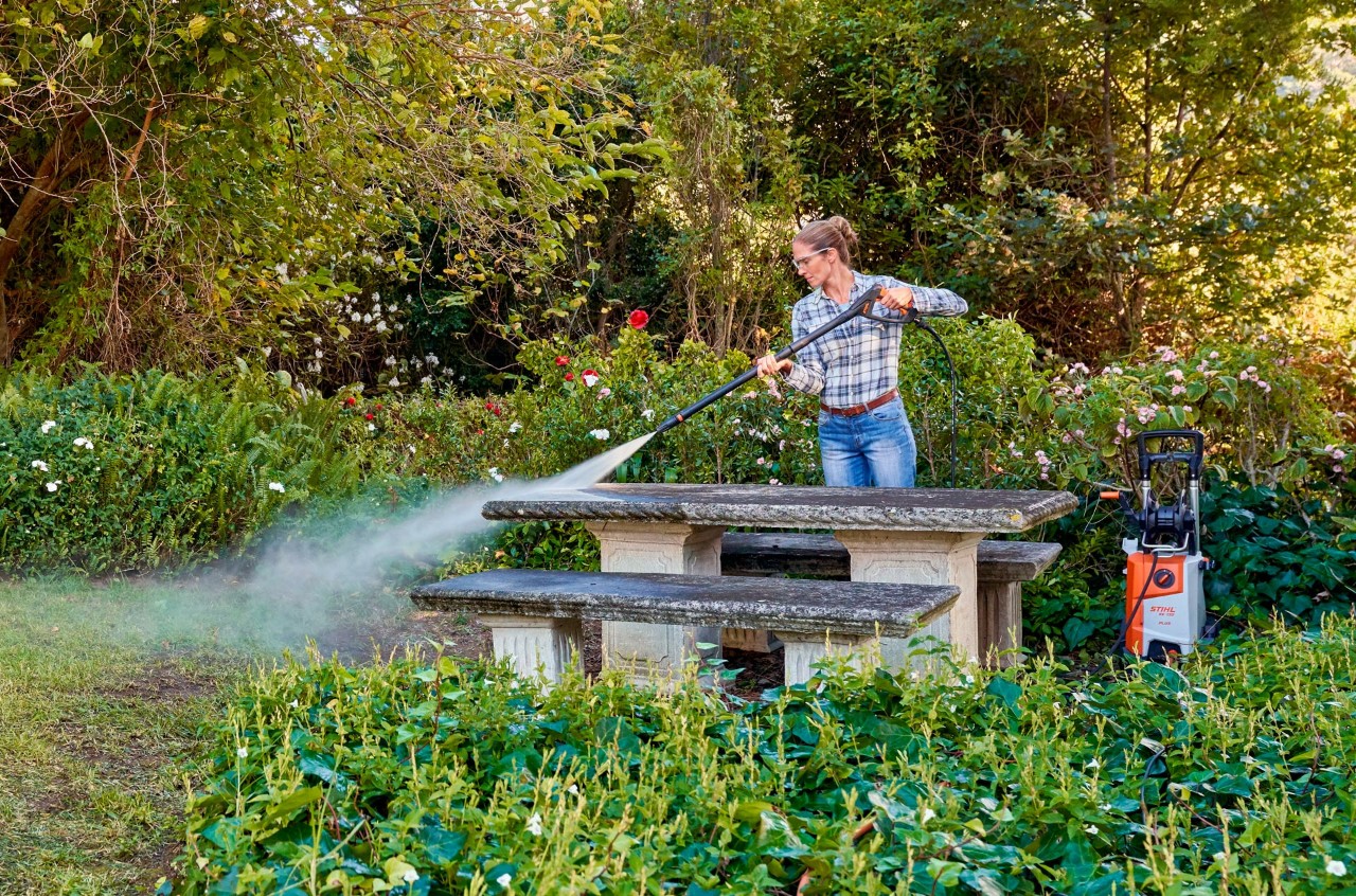 Frau reinigt Gartenmöbel im Garten mit einem STIHL Hochdruckreiniger.