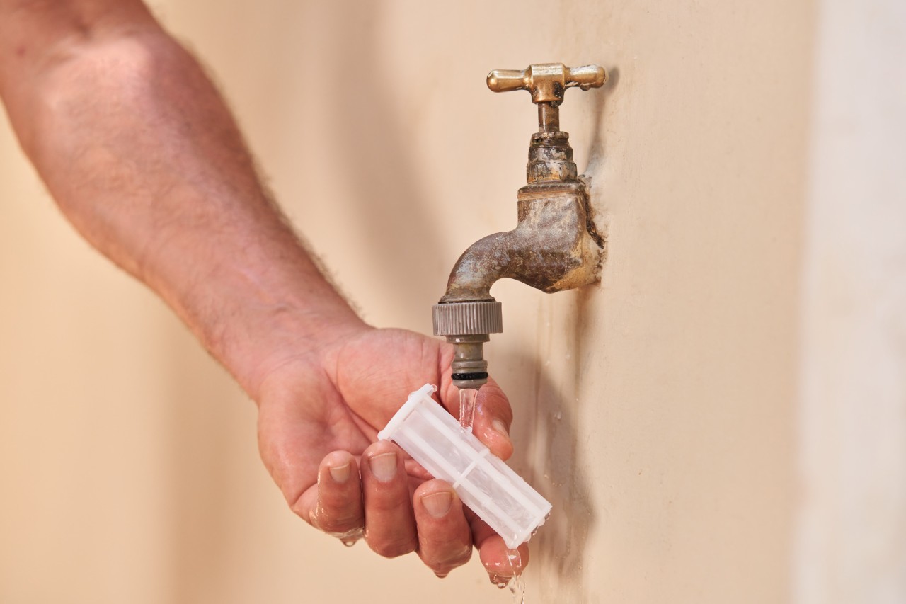 Eine Person reinigt einen Wasserfilter unter dem Wasserhahn