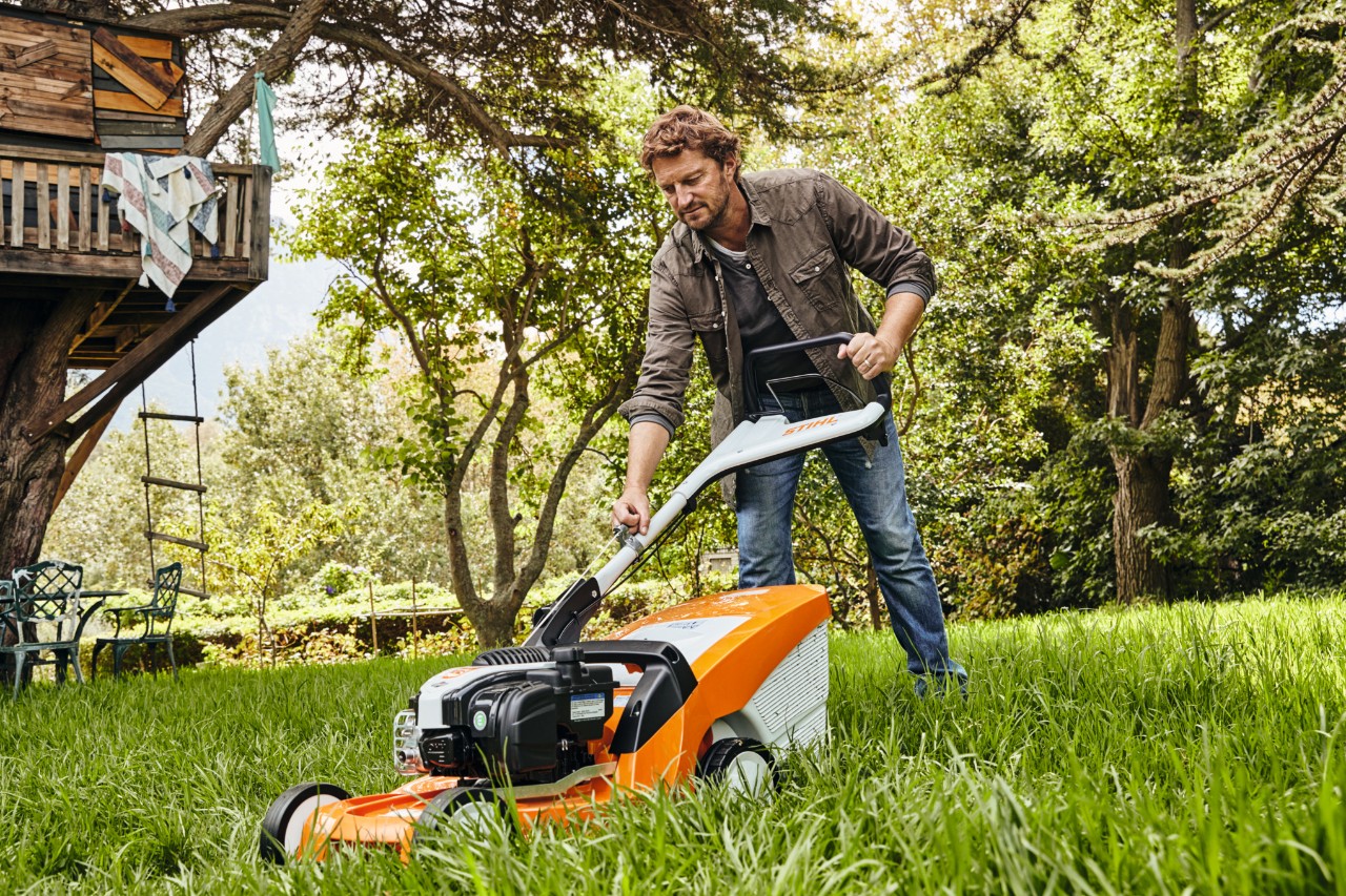 Ein Mann auf einer Gartenwiese zieht am Starterseil des Benzinrasenmähers STIHL RM 448 TC, um ihn zu starten