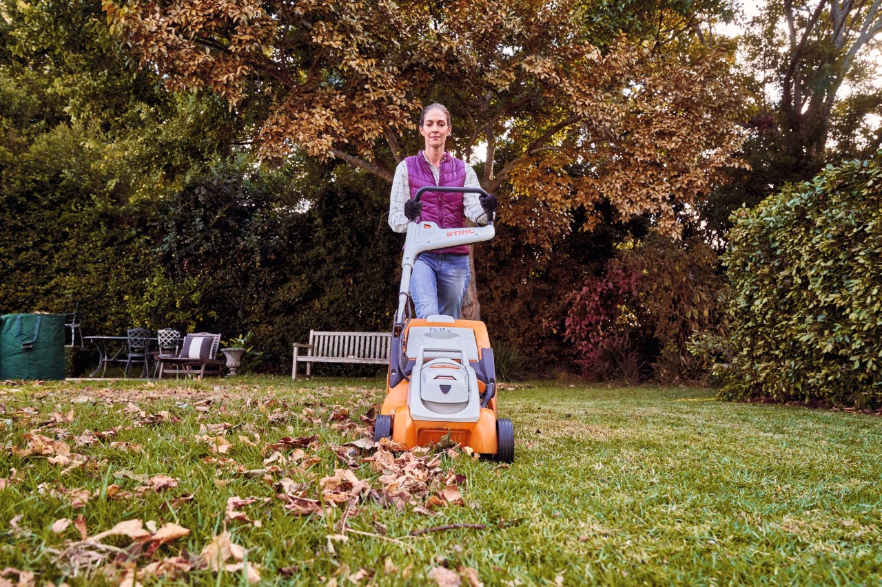 Eine Frau auf einem Gartengrundstück verwendet einen Rasenmäher zum Laubaufsammeln 