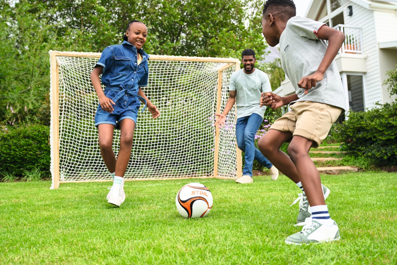 Drei Kinder spielen im Garten Fussball mit einem Fußballtor aus Holz