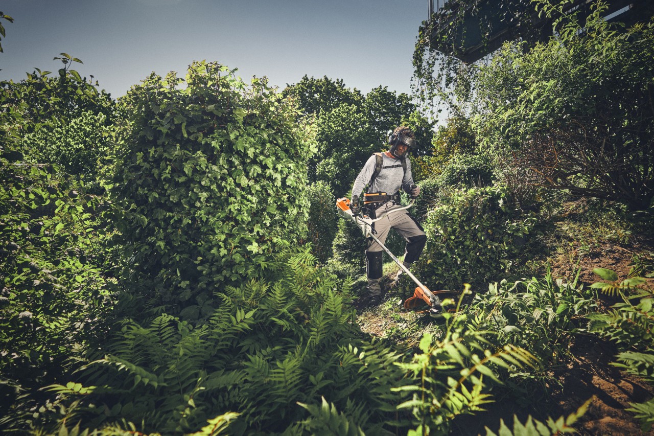 Une personne portant un équipement de protection coupe les broussailles sauvages à l'aide d'une débroussailleuse STIHL.