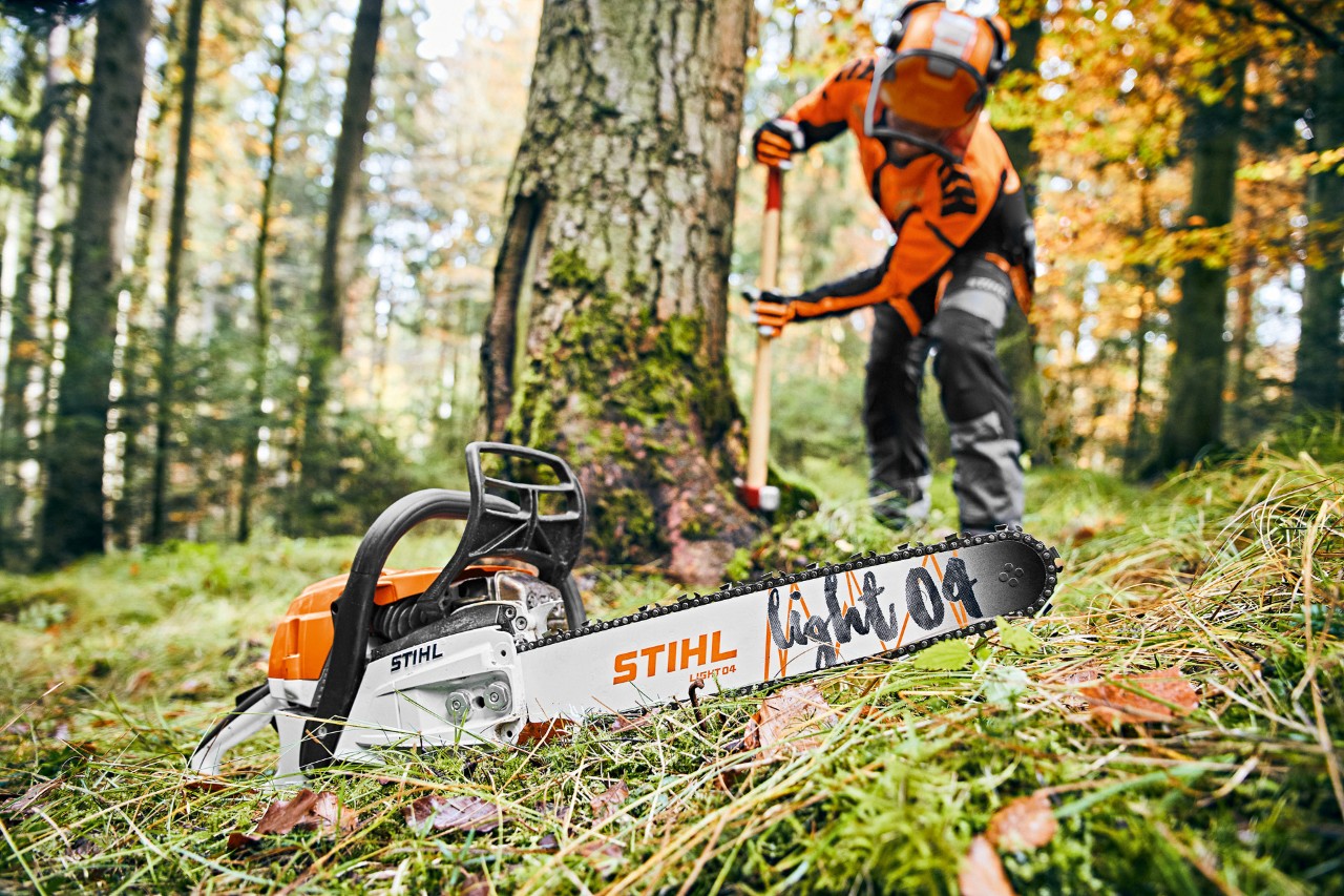 Homme en équipement de protection dans la forêt, au premier plan, tronçonneuse à essence STIHL MS 261 C-M avec guide-chaîne Light 04