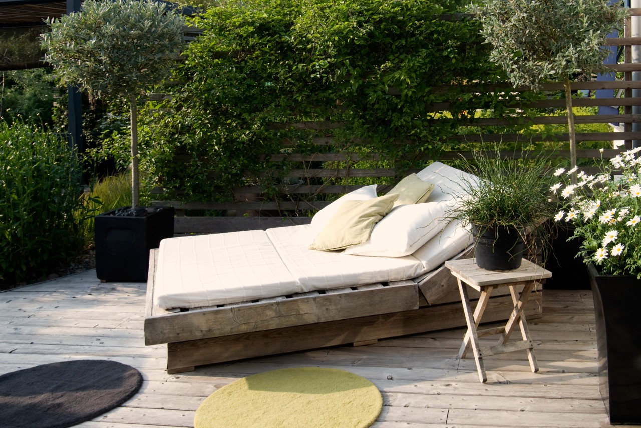 Oasis, espace détente, couchette d’extérieur dans un petit jardin, tapis ronds à l’avant, bacs à plantes tout autour, brise-vue.