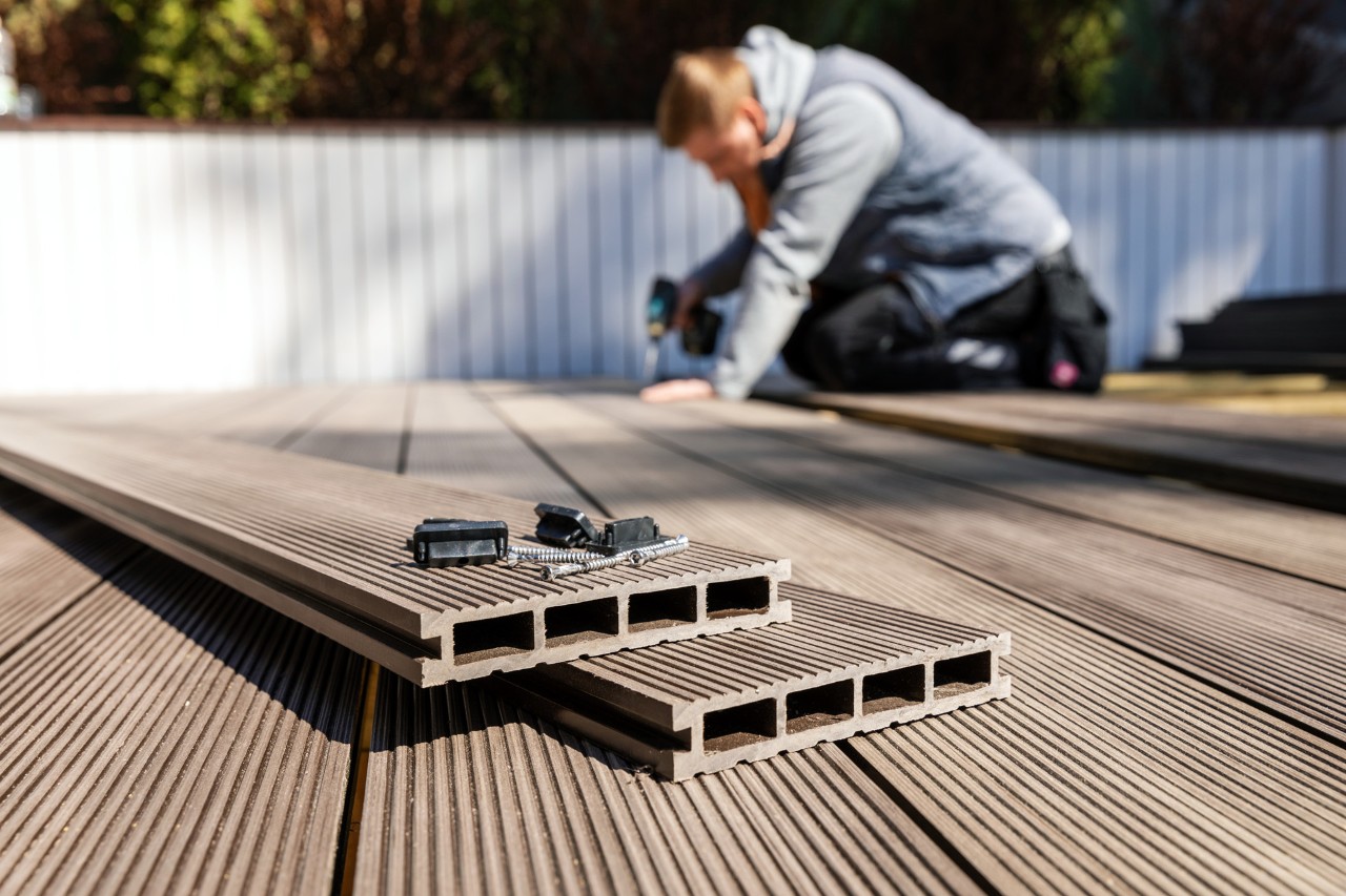 Homme posant un sol en bois composite sur une terrasse devant une clôture blanche