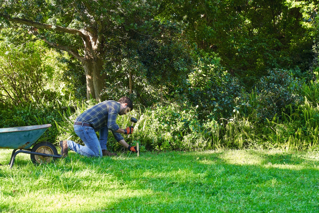 Un homme délimite la surface destinée à accueillir une prairie de fleurs sauvages à l’aide d’une corde à linge et de piquets