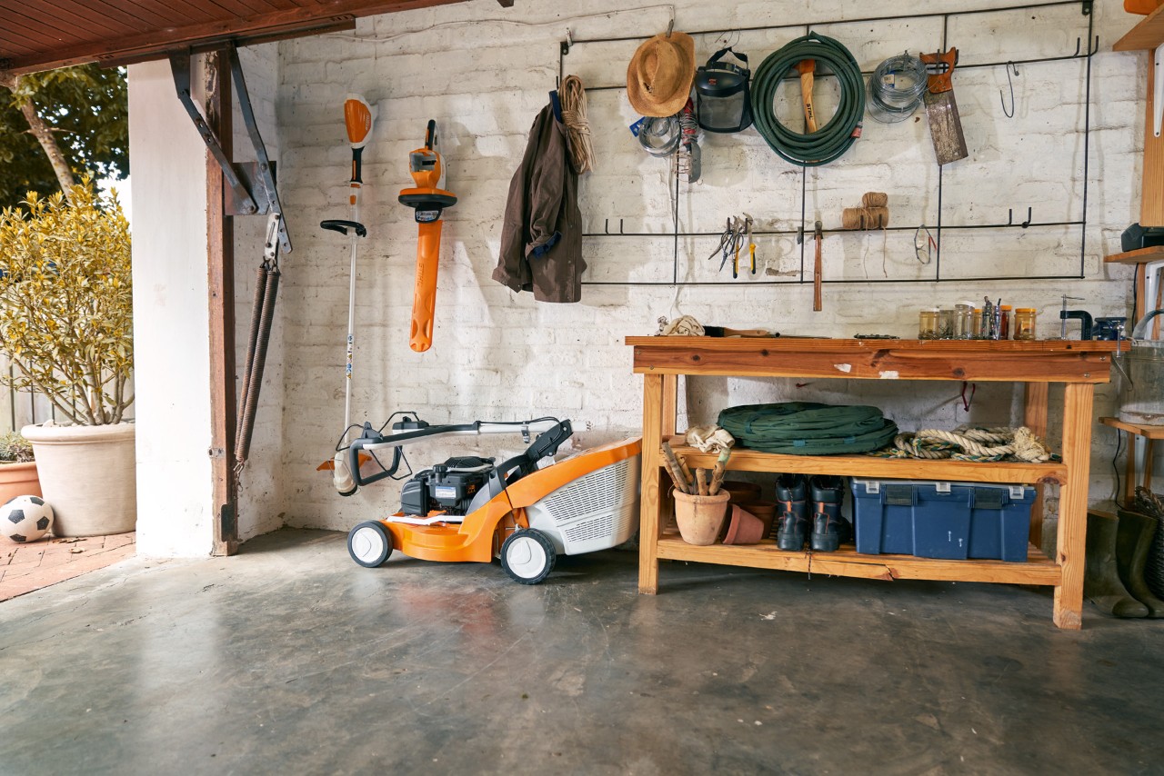 Une tondeuse à gazon à essence STIHL RM 448 TC et d’autres outils de jardin électriques rangés avec soin dans un garage