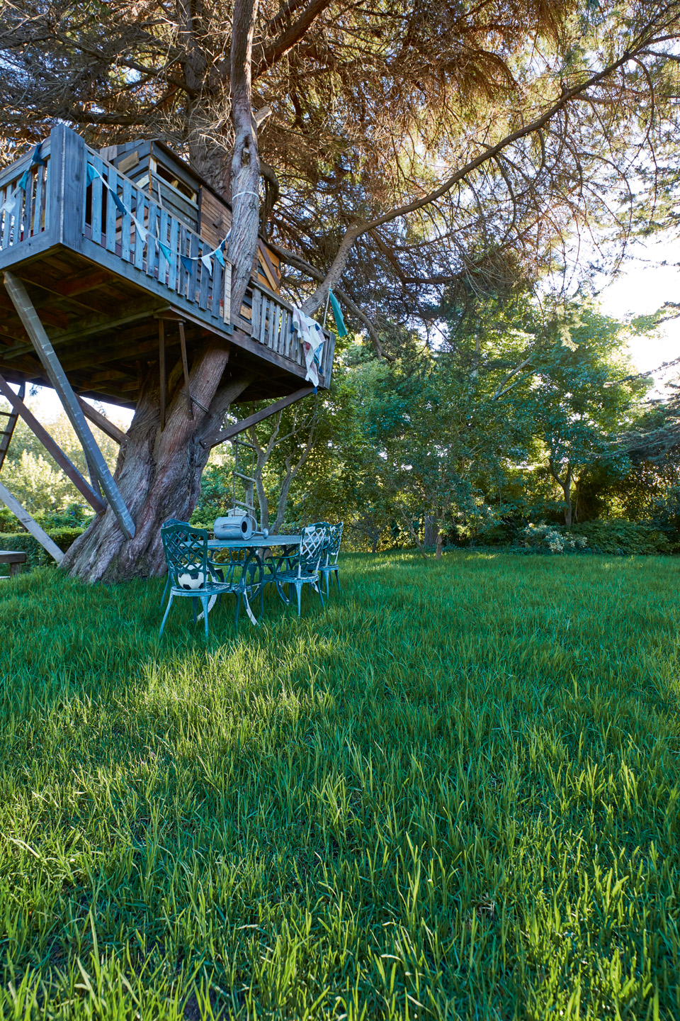 Arrosage du gazon : Un terrain verdoyant avec une cabane dans un arbre, une table et des chaises de jardin vertes et de grands arbres