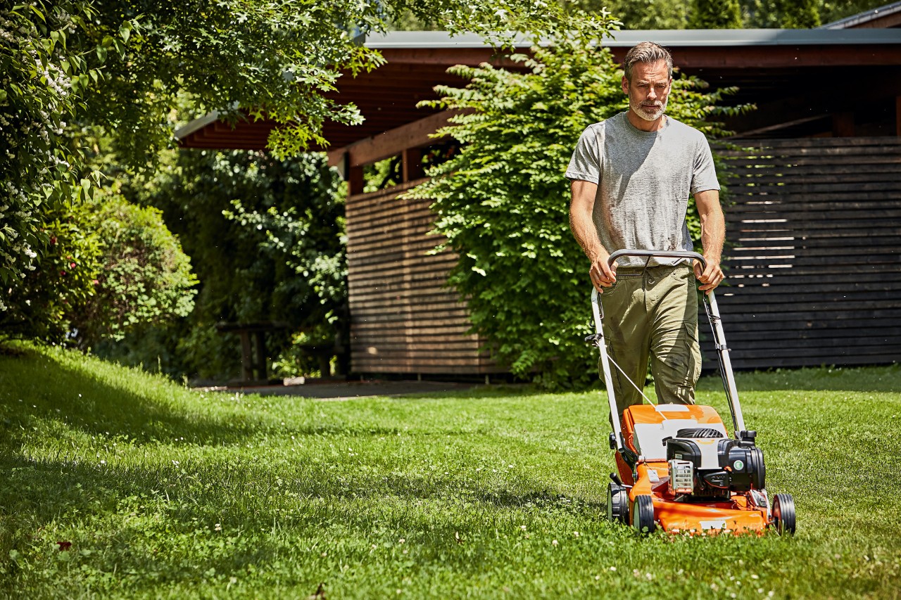  Homme tondant correctement sa pelouse avec une tondeuse à gazon thermique STIHL RM 248 devant une cabane de jardin