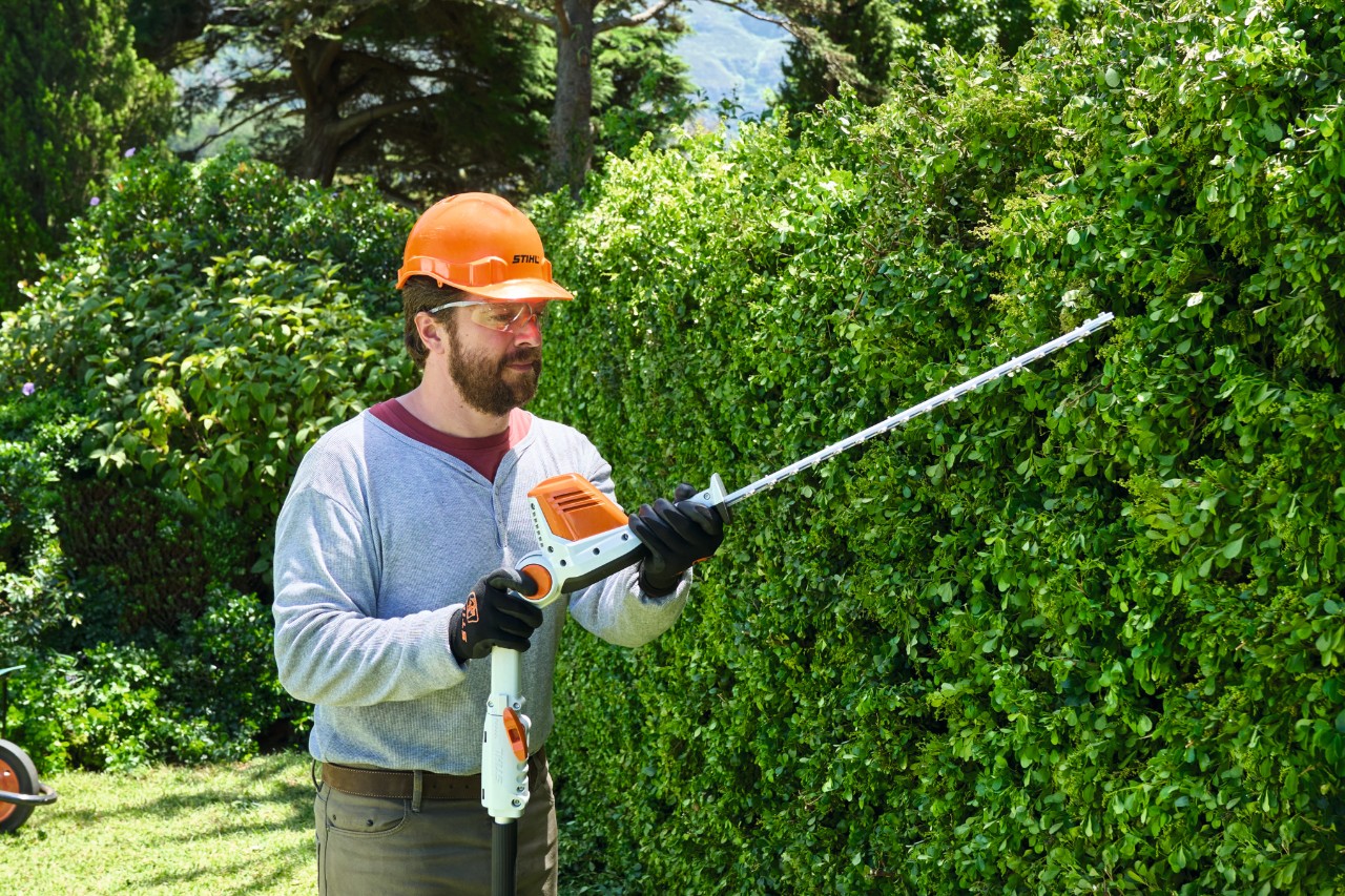 Un homme en équipement de protection taille une haie haute avec un taille-haie à batterie STIHL HLA 56