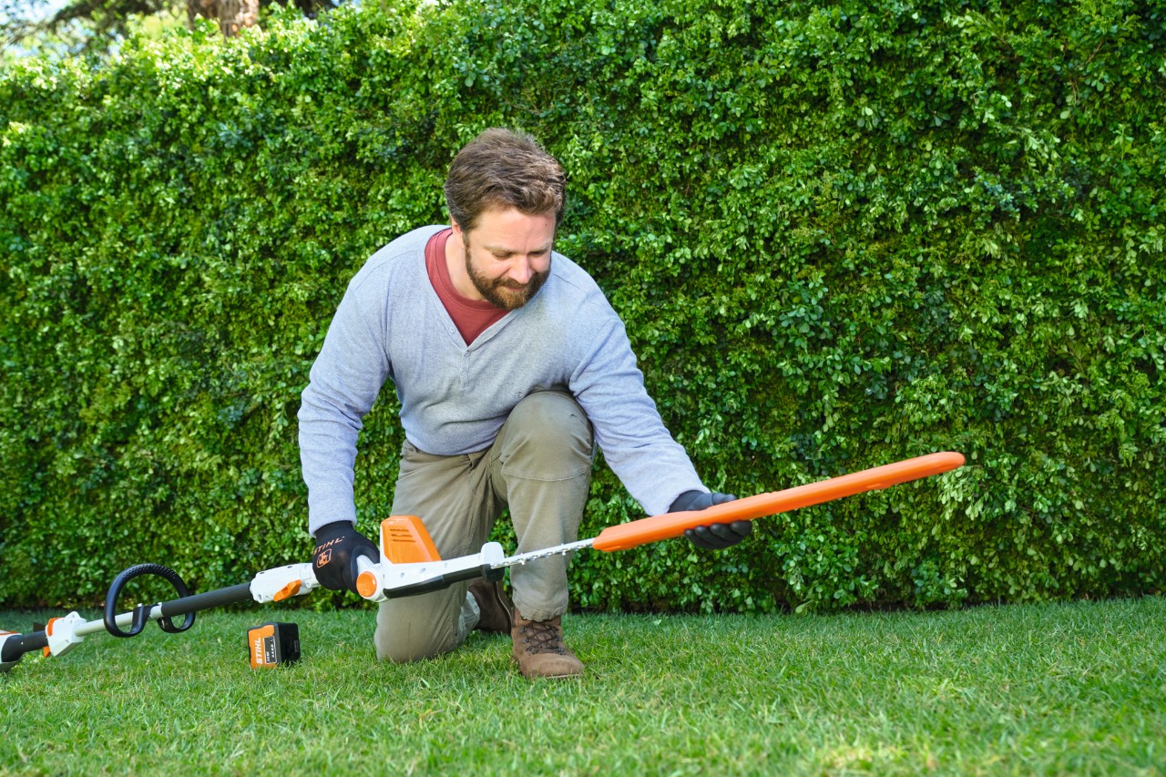 Un homme devant une haie dépose un taille-haie à batterie STIHL HLA 56 sur le gazon