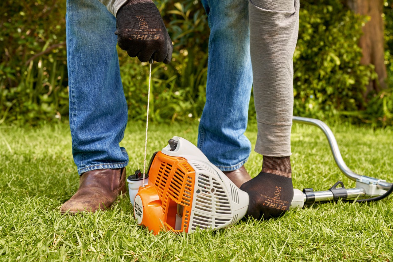 Un homme tirant sur le câble de démarrage de la débroussailleuse à essence STIHL FS 56 