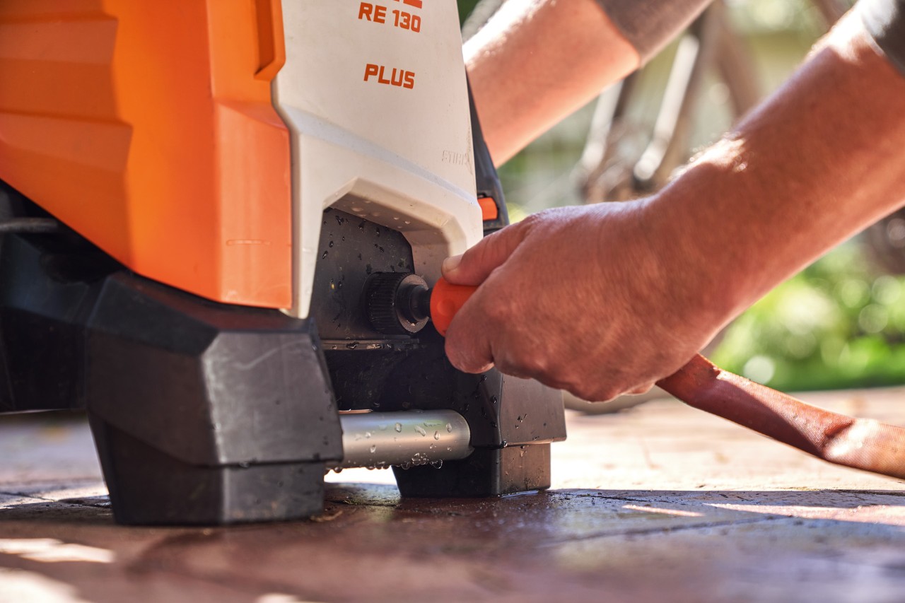 Une personne raccordant un tuyau d’arrosage au nettoyeur haute pression STIHL RE 130 PLUS en vue de son utilisation