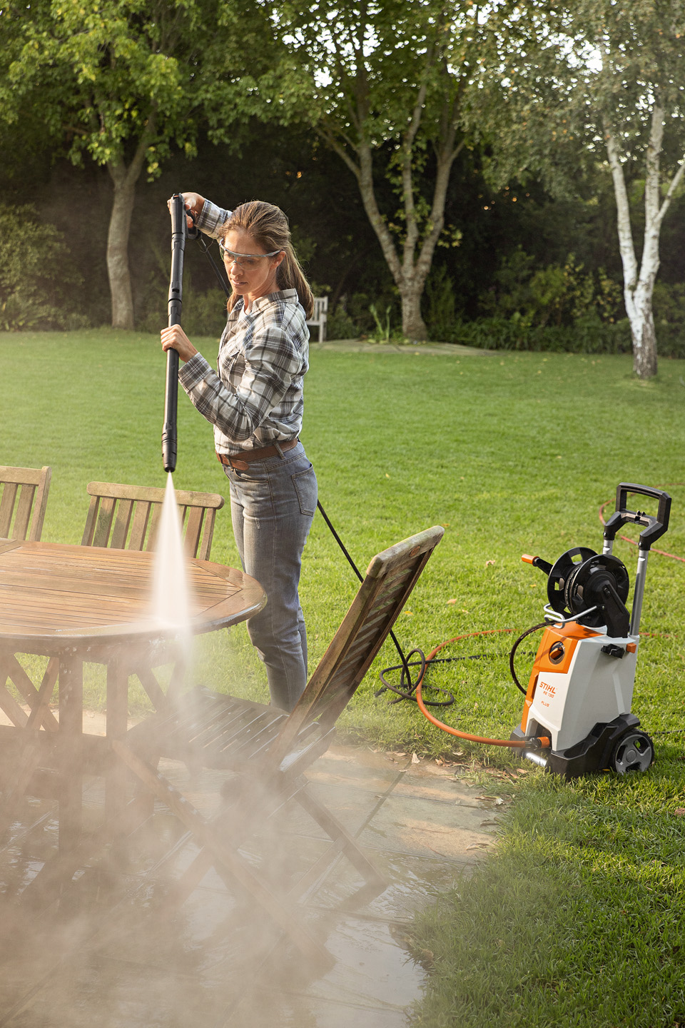 Une femme utilisant le nettoyeur haute pression STIHL RE 130 PLUS à l’extérieur pour nettoyer des meubles de jardin