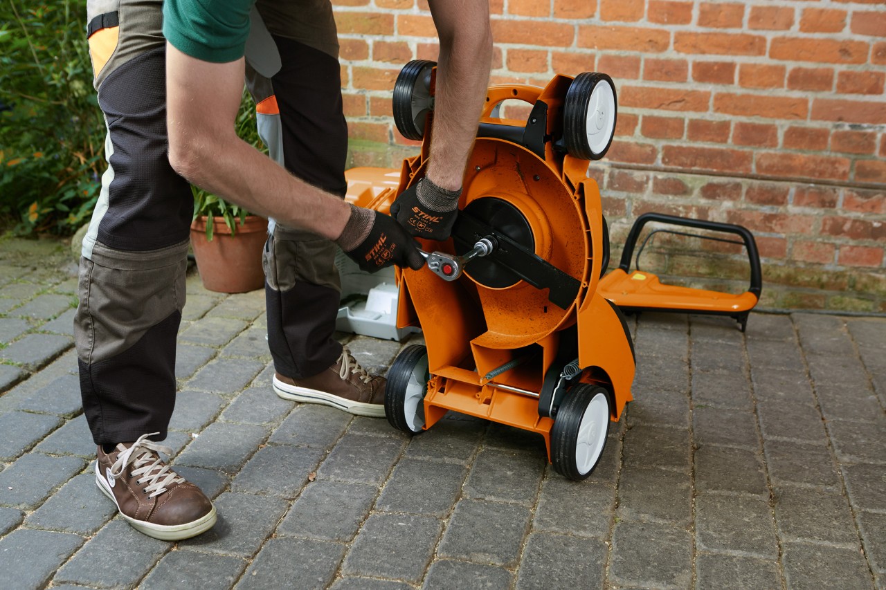 Une personne équipée de gants qui retire la lame d’une tondeuse à gazon STIHL