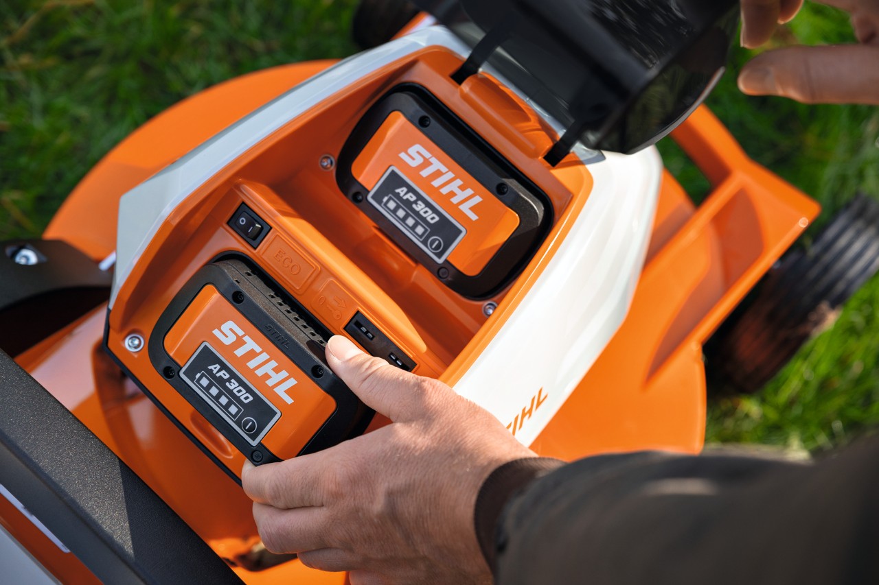 Une personne en train de placer une batterie entièrement chargée STIHL AP 300 dans une tondeuse à gazon