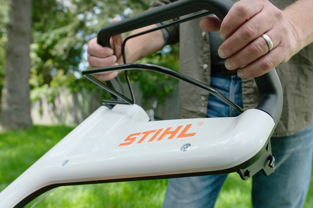 Une personne en train de pousser l’arceau de coupure du moteur d’une tondeuse à gazon STIHL