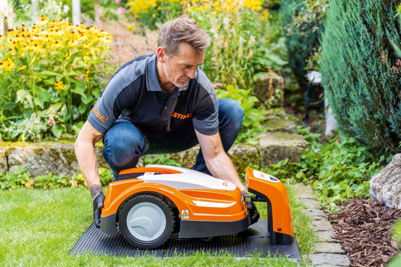 Un revendeur STIHL place un robot de tonte STIHL iMOW dans sa station de charge dans un jardin