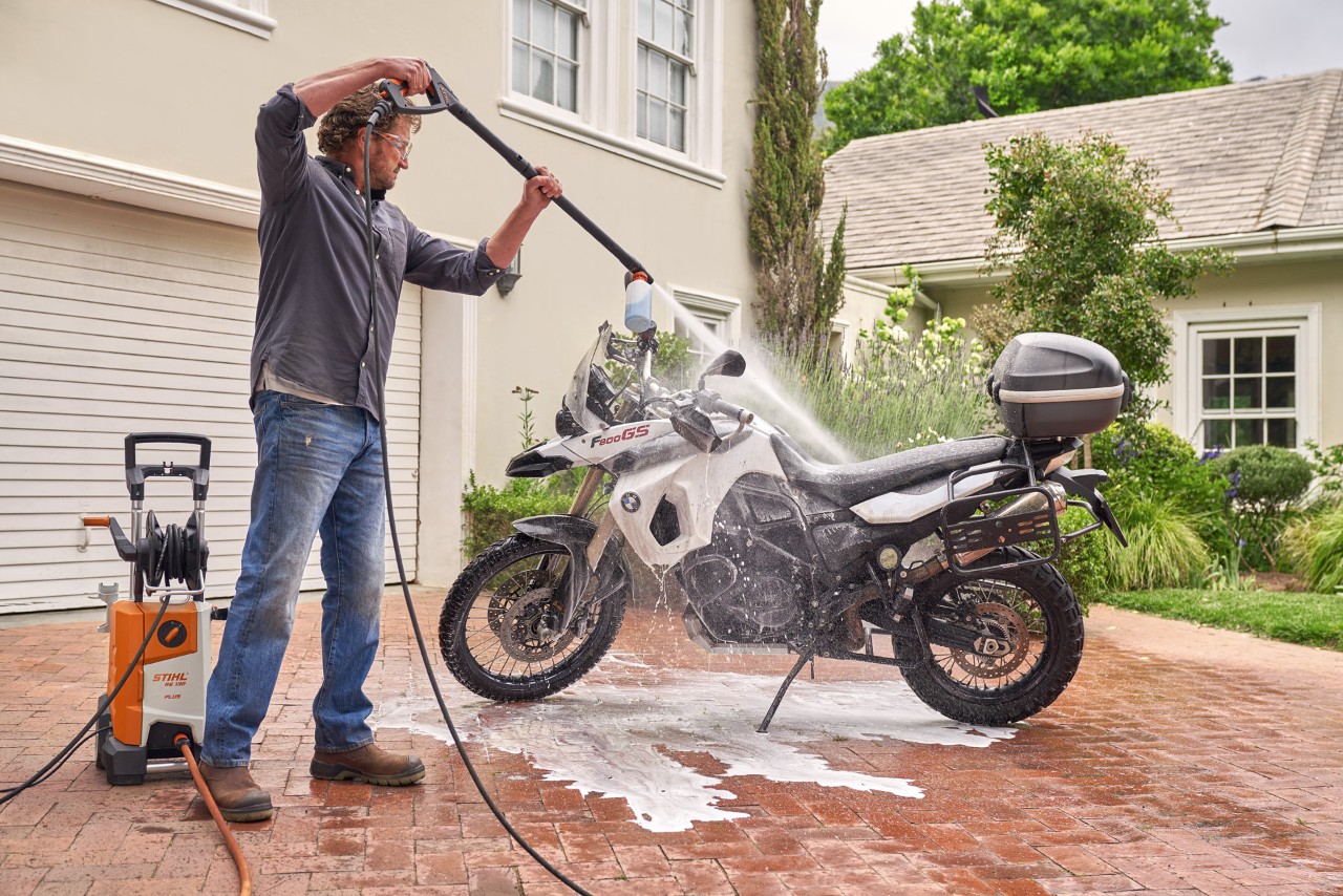 Homme utilisant le nettoyeur haute pression STIHL RE 130 Plus pour vaporiser le shampooing pour véhicules sur une moto