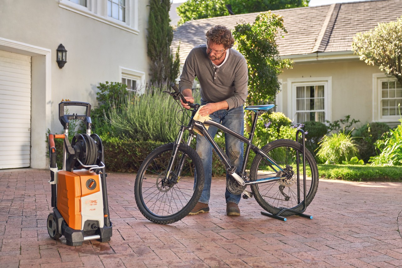 Homme séchant un vélo avec un chiffon, avec un nettoyeur haute pression STIHL RE 130 Plus placé à côté de lui