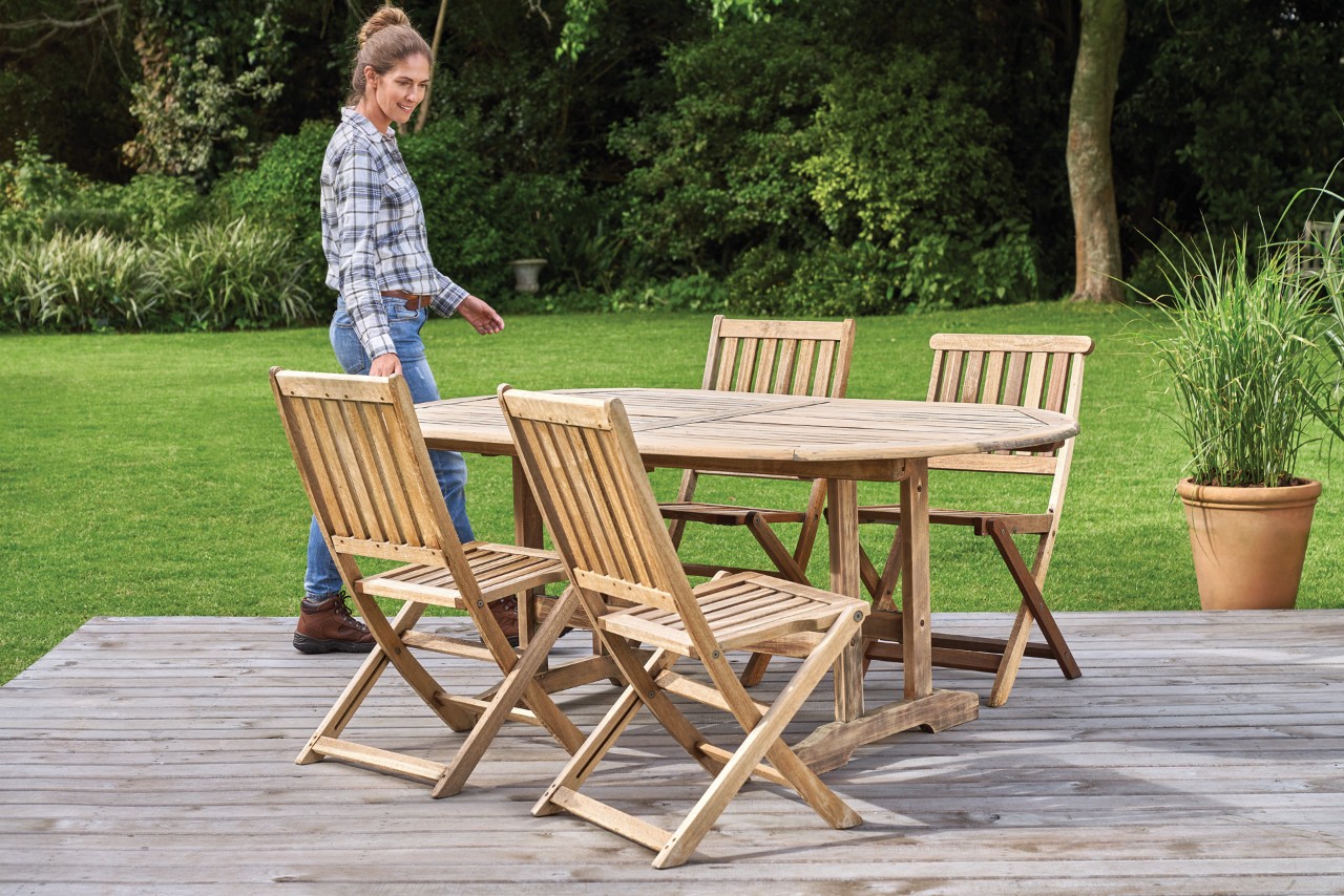 Femme devant un salon de jardin en bois propre sur une terrasse, avec un nettoyeur haute pression STIHL RE 130 Plus 