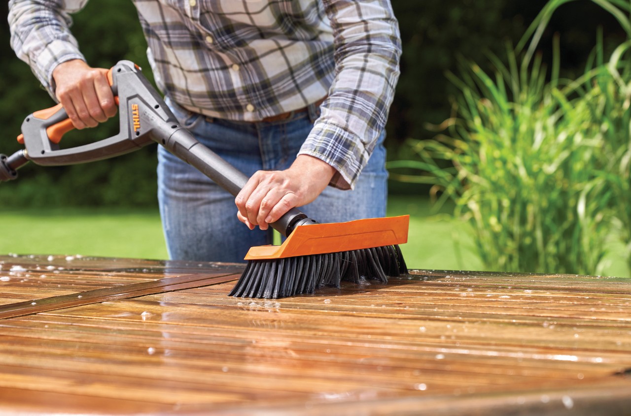 Femme nettoyant une table de jardin en bois avec un nettoyeur haute pression STIHL RE 130 Plus avec brosse de lavage