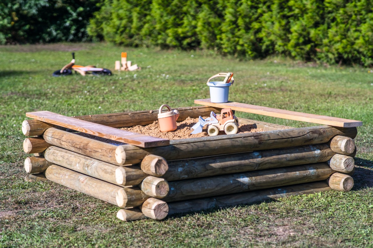 Bac à sable artisanal avec des jouets en plastique sur une parcelle de jardin