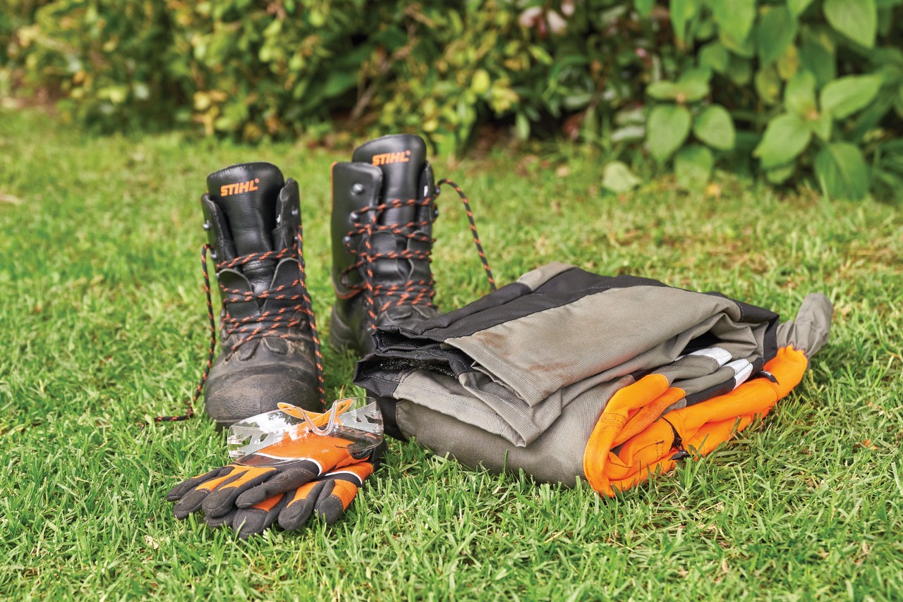 Bottes, gants de protection et pantalons de protection contre les coupures disposés sur l’herbe