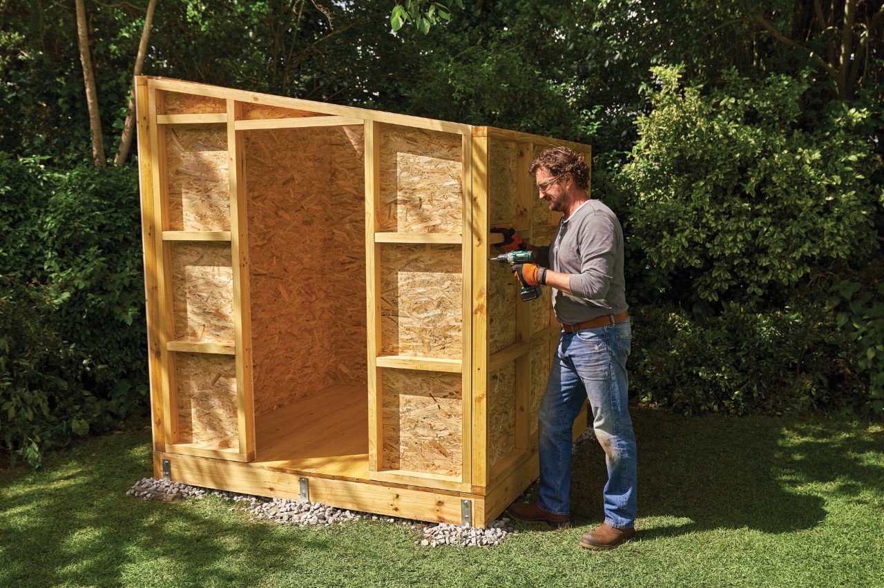 Comment construire un abri de jardin : homme vissant les parois assemblées d’un abri de jardin