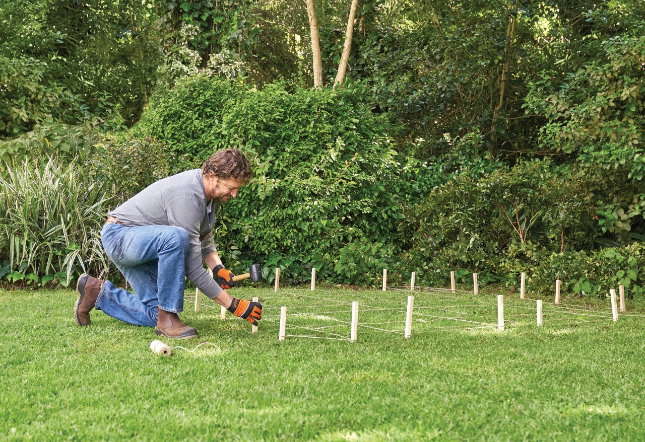 Comment construire un abri de jardin : homme délimitant les contours d’un abri de jardin sur la pelouse