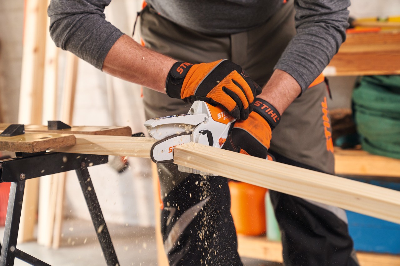 Une personne portant des gants de protection STIHL Function&nbsp;Protect en train de couper des baguettes de cadre pour le brise-vue avec la scie de jardin STIHL&nbsp;GTA&nbsp;26