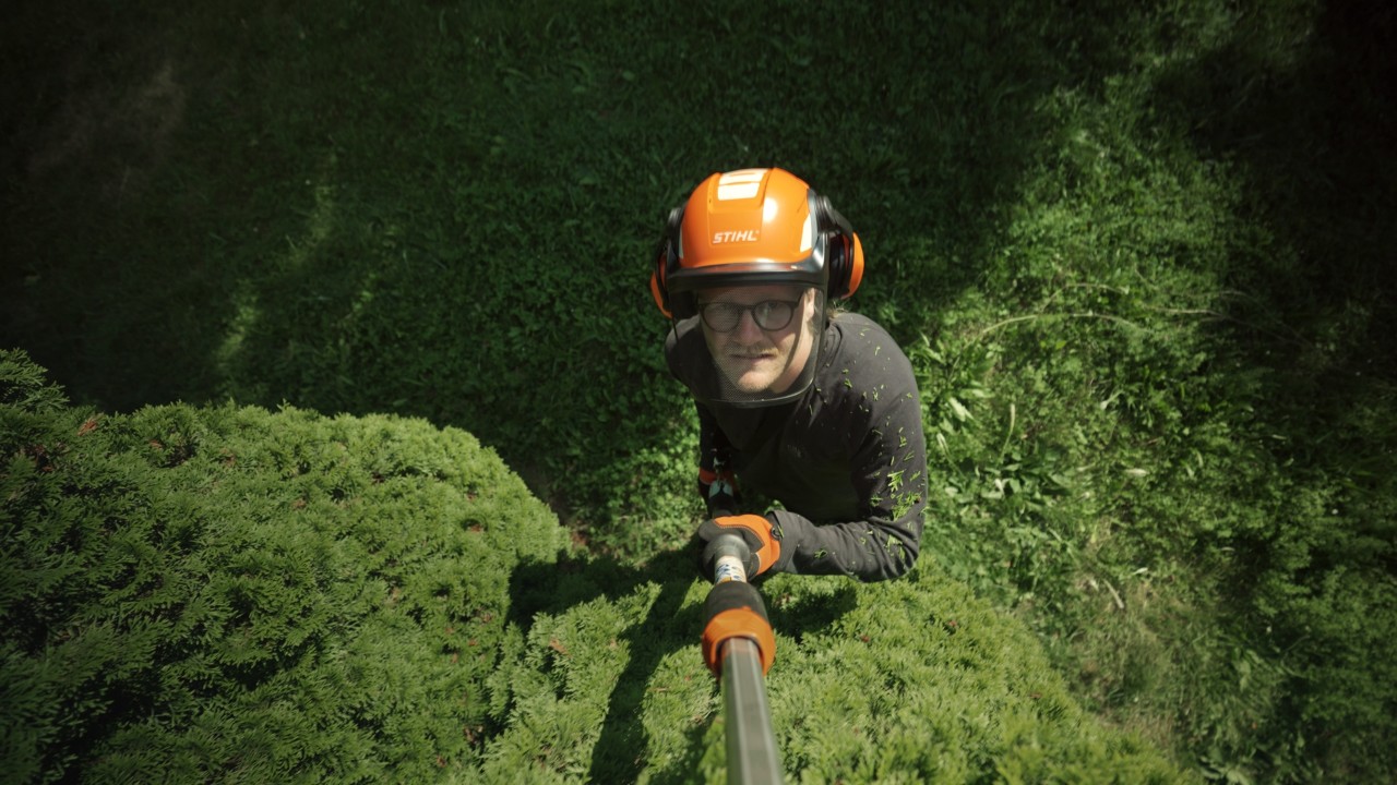 Achille coupe des branches dans un arbre avec un élagueur sur perche, travaux de jardinage dans la verdure, campagne Real People. STIHL People.