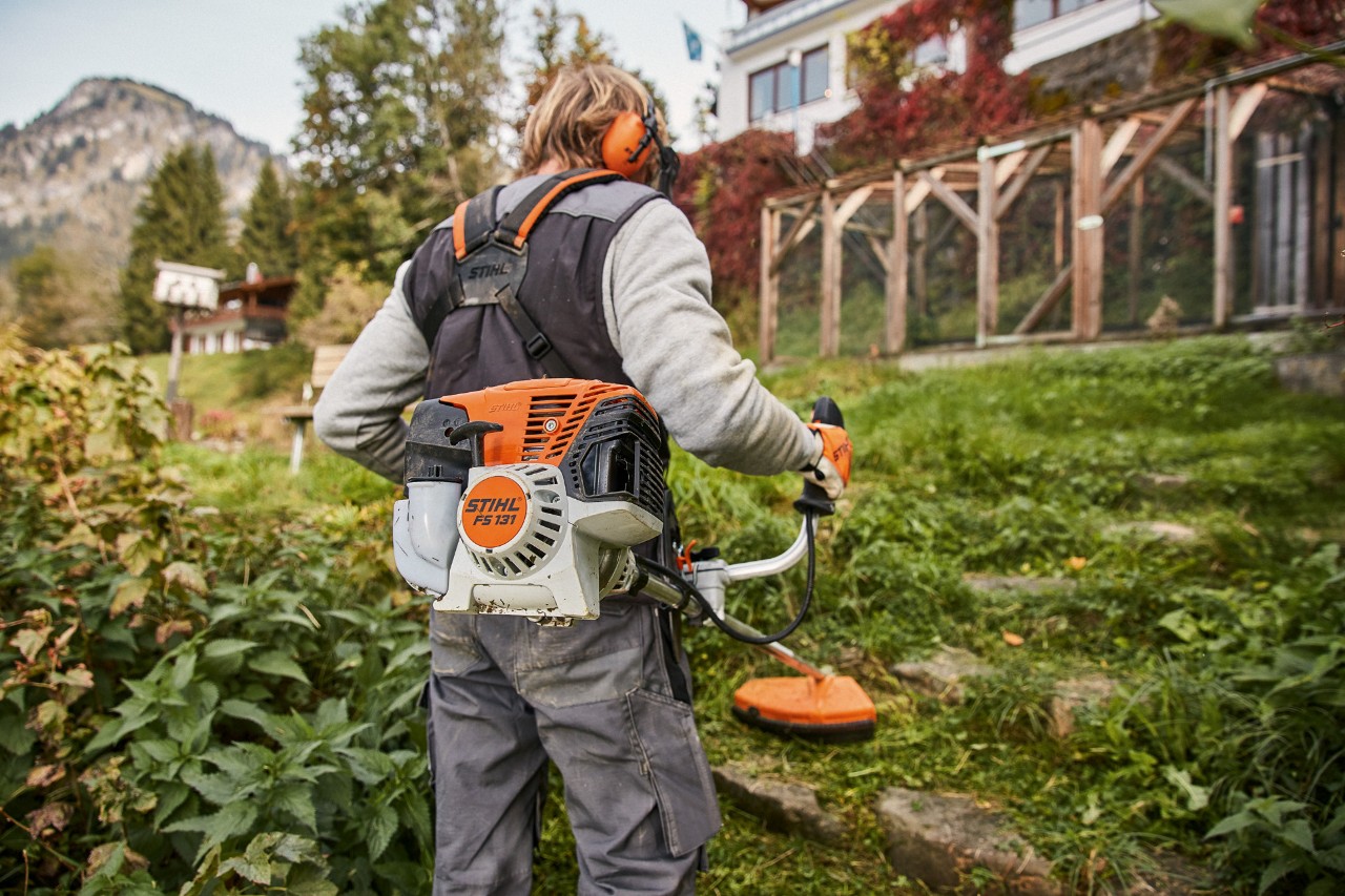 Un terrain en pente devant une maison est tondu avec la débroussailleuse STIHL FS 131 avec moteur 4-Mix®.