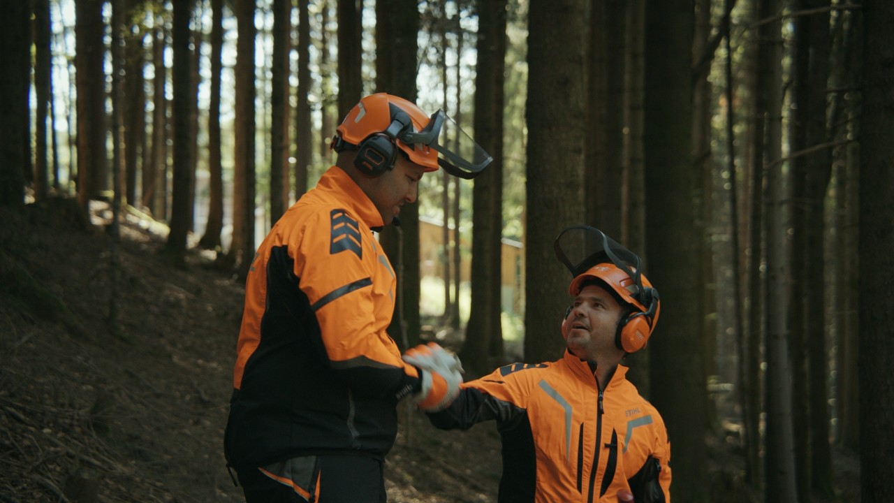 Daniel e un amico nel bosco mentre si danno il cinque dopo il lavoro del legno, con dispositivi di protezione STIHL, Real People. STIHL People.