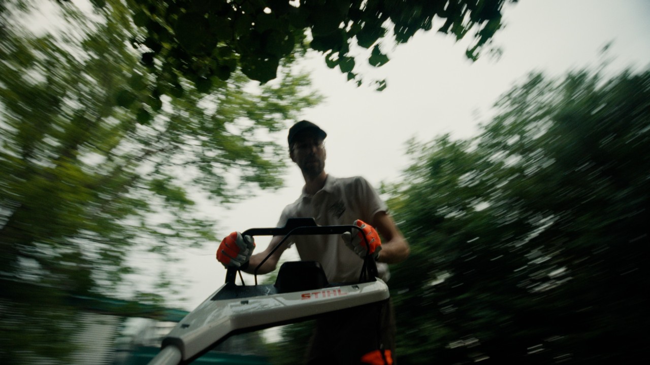 Patrick mentre taglia l’erba, ripresa dinamica con leggero effetto di movimento all’aperto