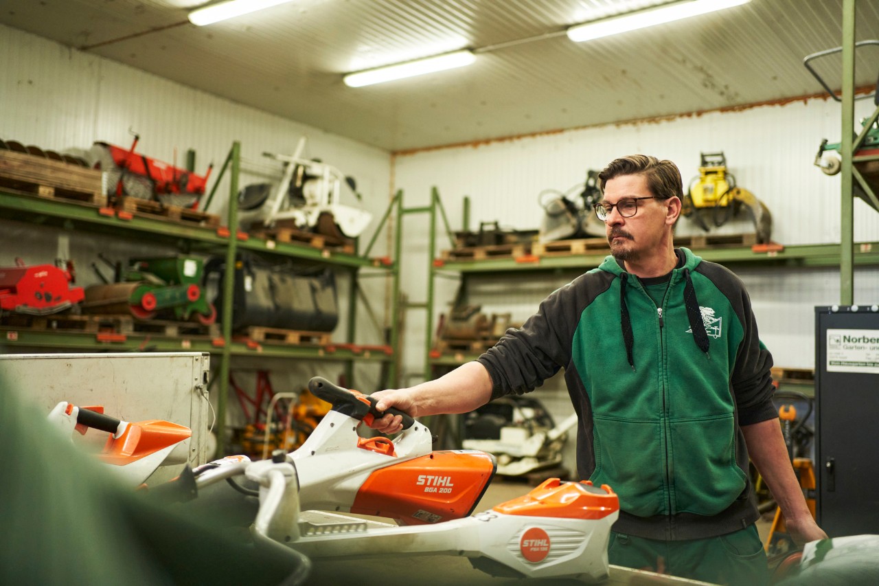 Un uomo in un'officina dietro un'area di lavoro con utensili a batteria STIHL che afferra il soffiatore a batteria STIHL BGA 200