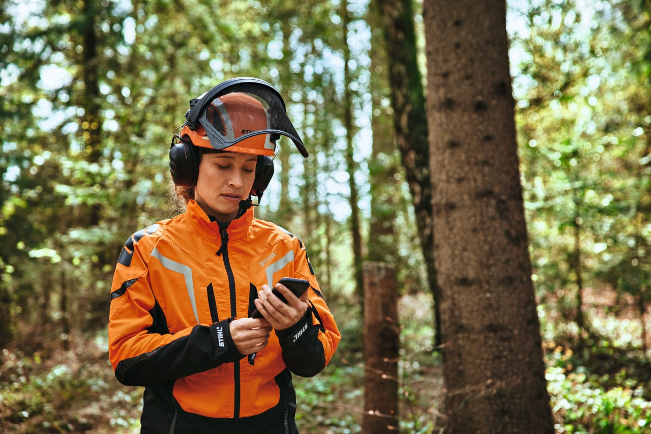 Donna munita di dispositivi di protezione individuale che utilizza uno smartphone nel bosco