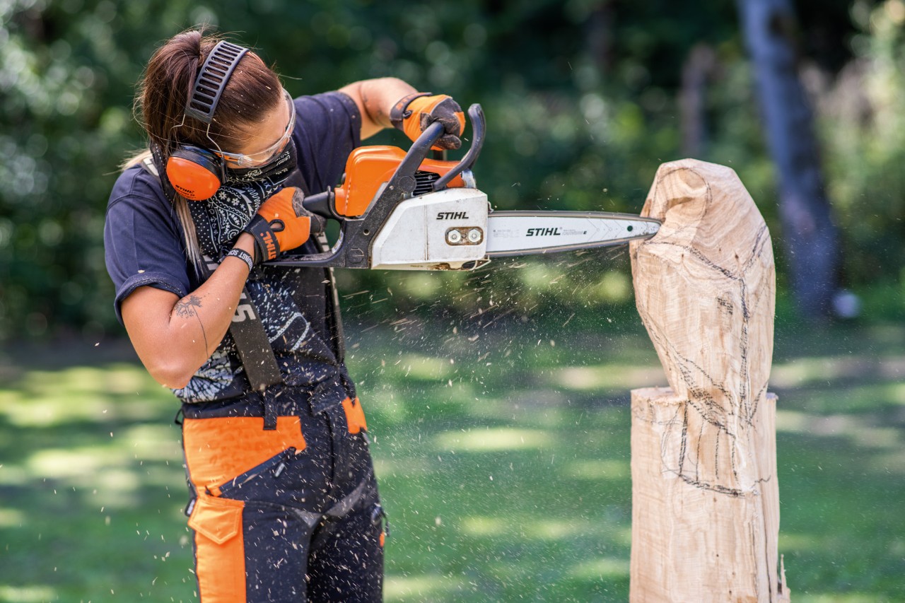 Donna che indossa una protezione acustica STIHL mentre intaglia con la motosega un gufo di legno