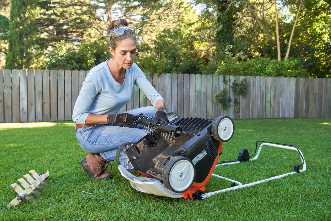 Donna con occhiali di protezione e guanti da lavoro che sostituisce l'unità di scarificazione dell'arieggiatore a batteria STIHL RLA 240