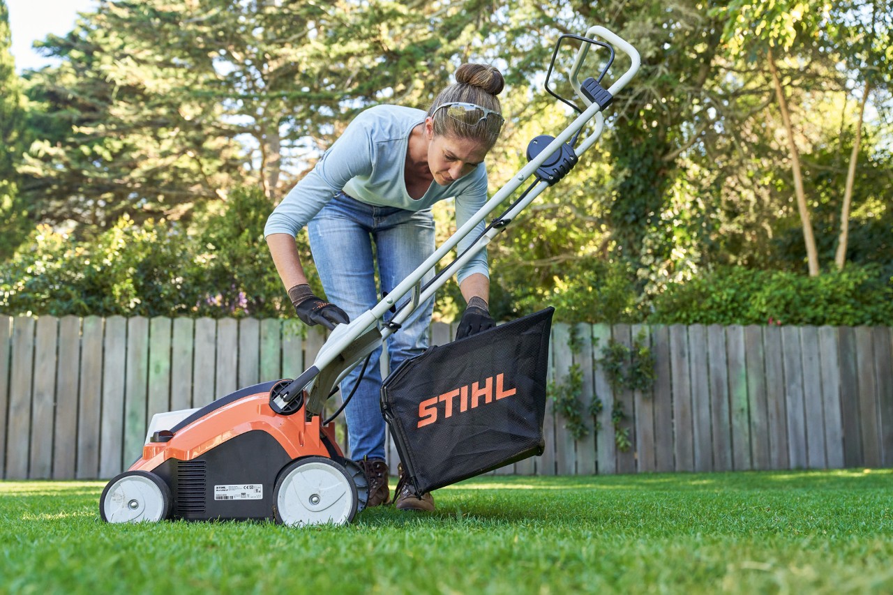 Donna che aggancia il cesto di raccolta dell'arieggiatore a batteria STIHL RLA 240 sul retro dell'attrezzo.