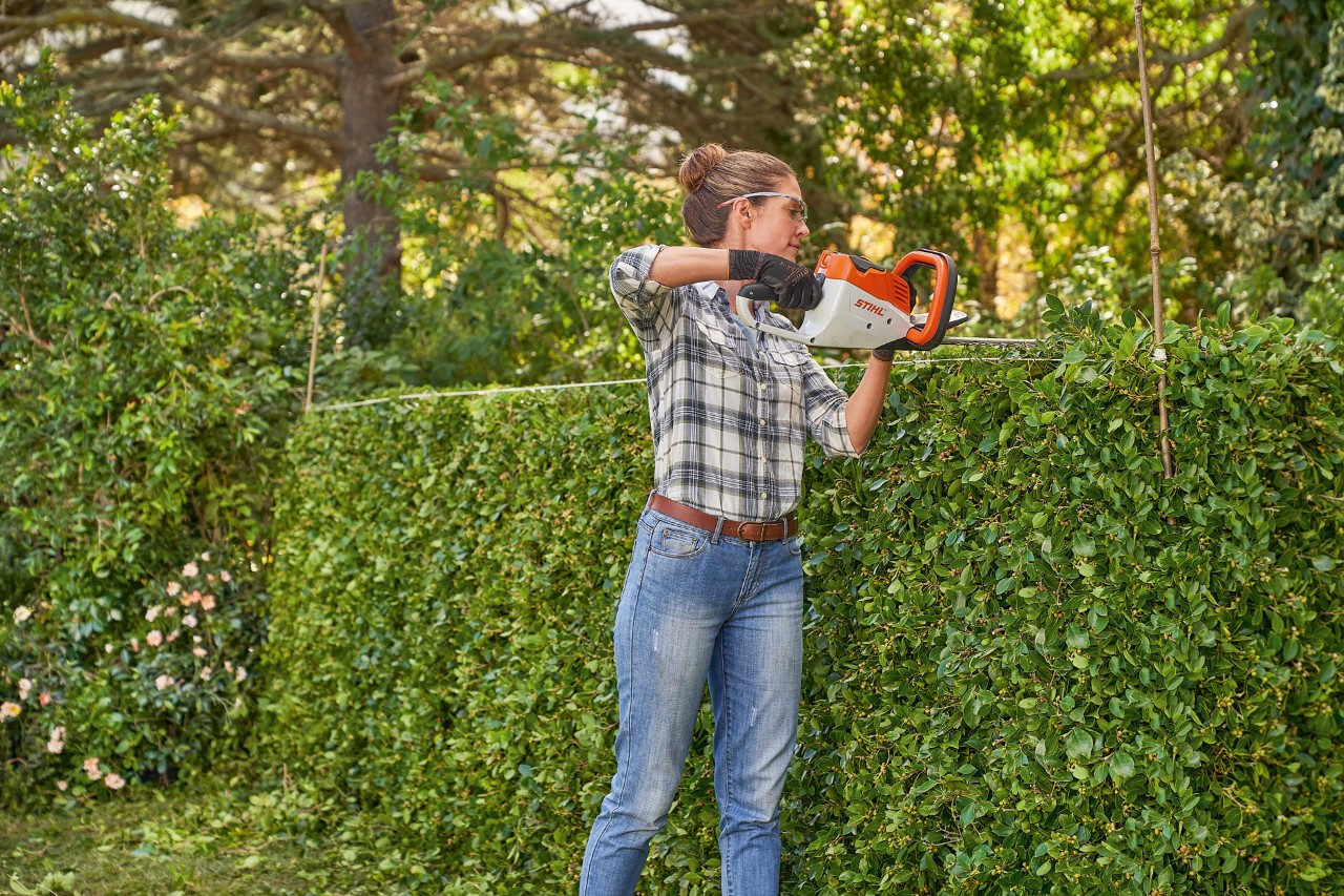 Una donna utilizza il tagliasiepi a batteria HSA 45 STIHL per sagomare una siepe