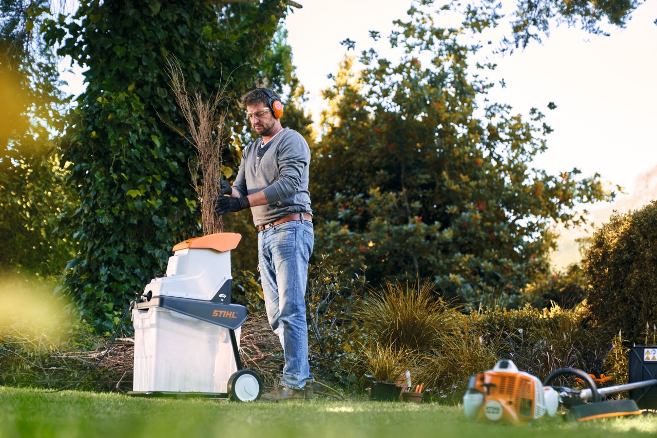 Uomo che utilizza un biotrituratore a benzina STIHL tra gli alberi e i cespugli davanti a un'abitazione