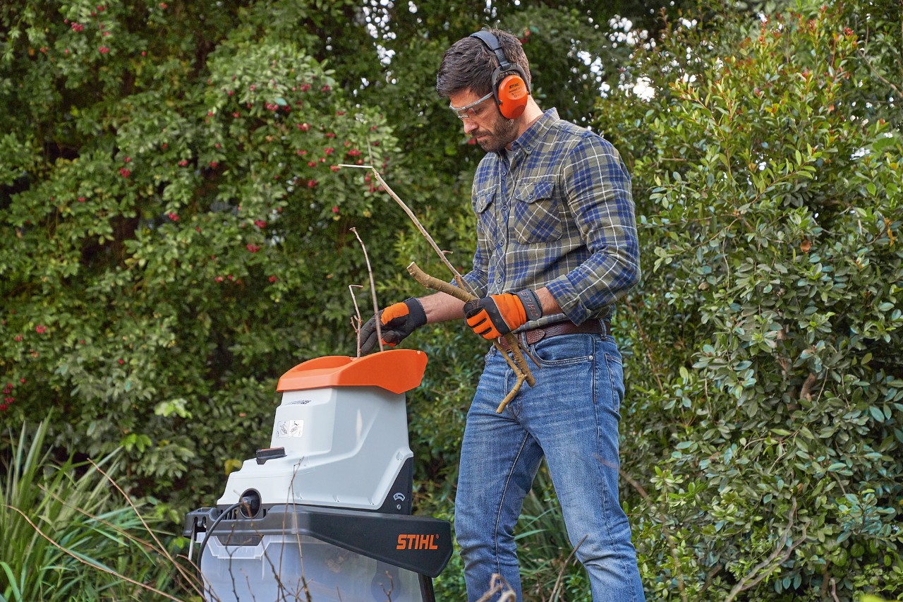 Uomo munito di dispositivi di protezione individuale che tritura dei rami con un biotrituratore STIHL
