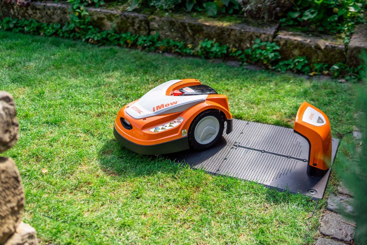 Robot tosaerba STIHL iMOW® accanto alla docking station su prato verde 